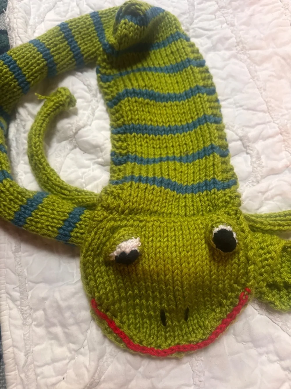 Soft, playful green striped knit scarf with blue accents. Designed with a frog h